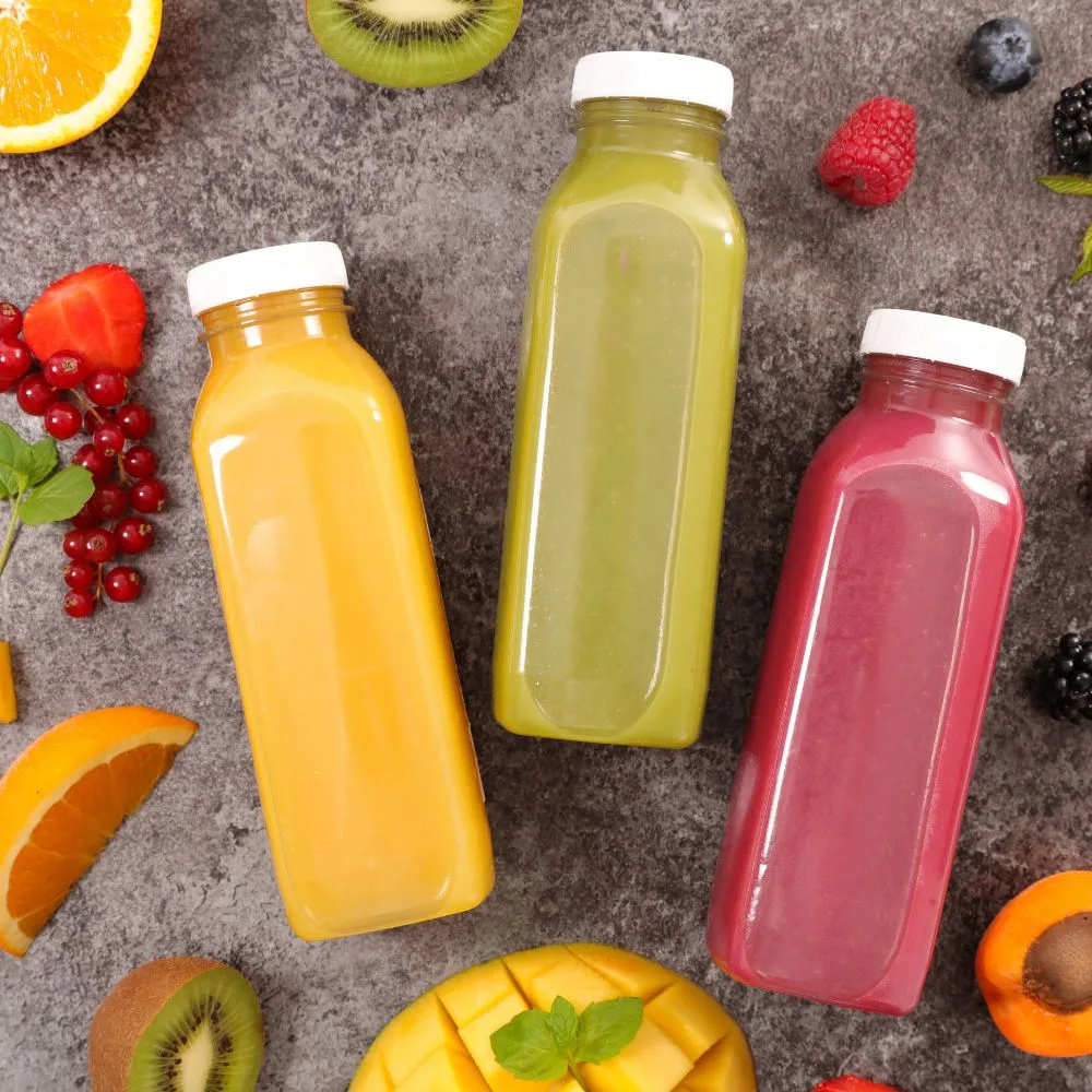 Square PET juice bottles with white caps in a flat-lay with fresh fruit — real production bottles, CupsPak