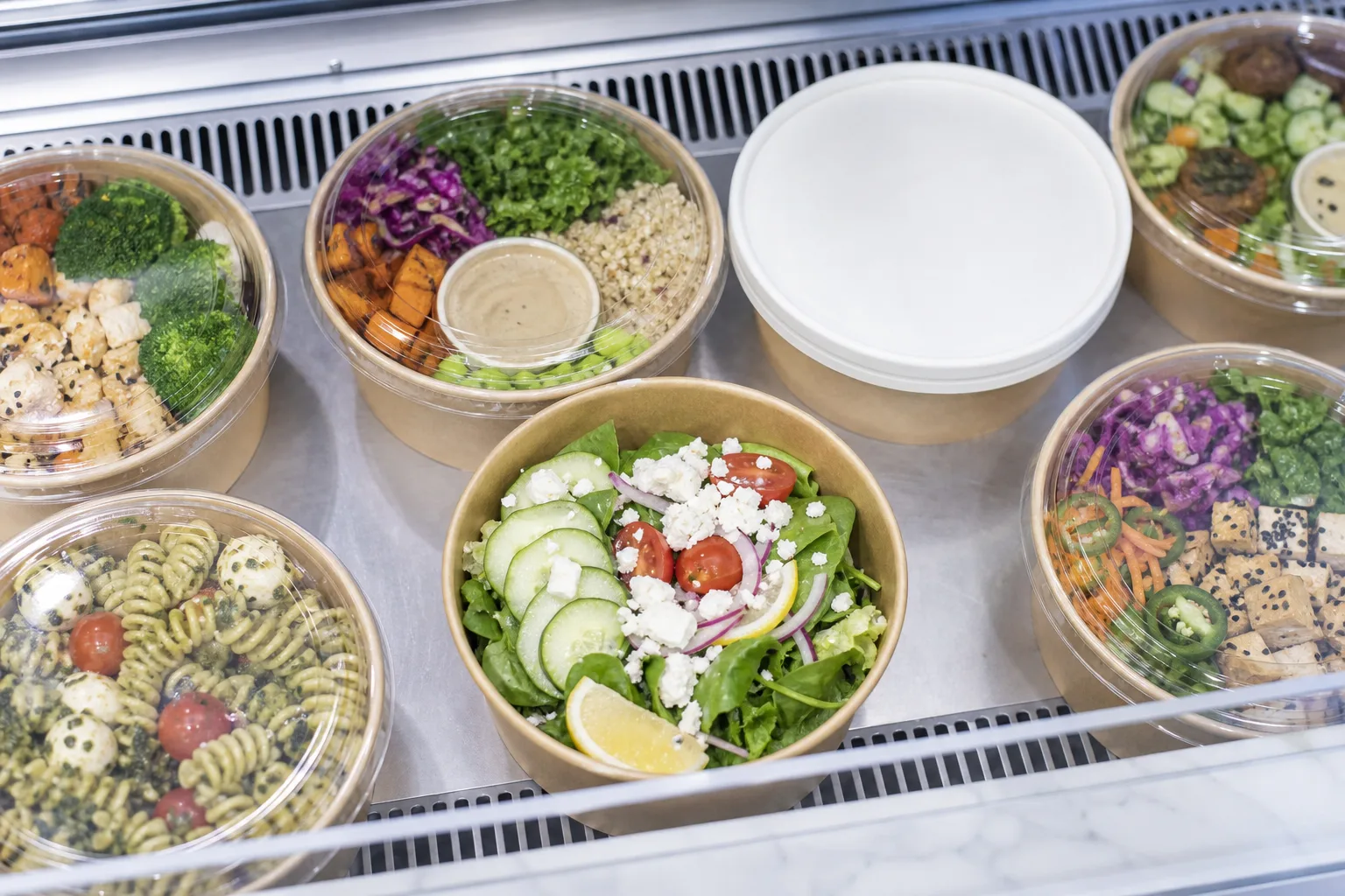 Kraft paper bowls with clear and paper lids in a refrigerated grab-and-go deli case