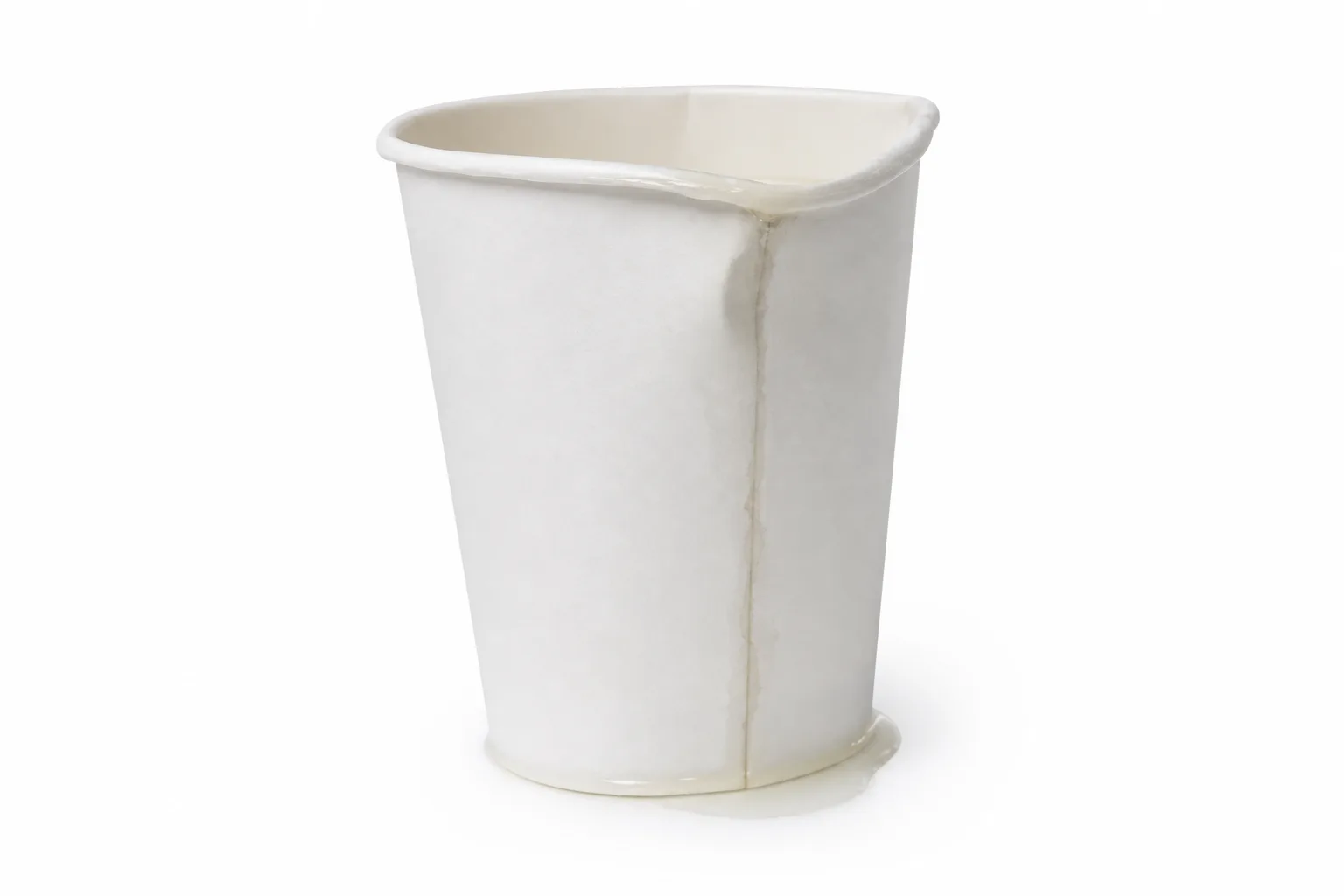 A white paper cup after microwave heating: the rim has buckled, a damp line runs down the vertical side seam, and liquid has pooled at the base