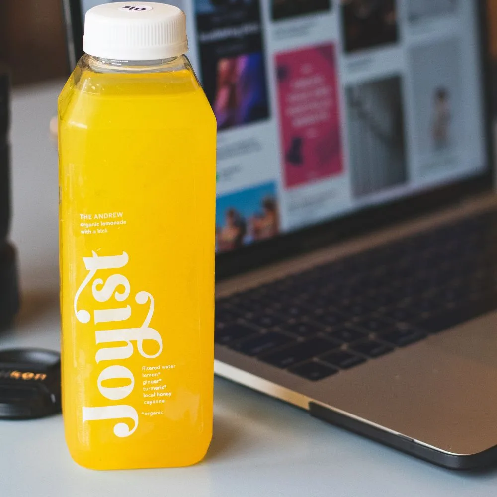 Branded screen-printed PET juice bottle in real use on a desk — CupsPak custom bottles